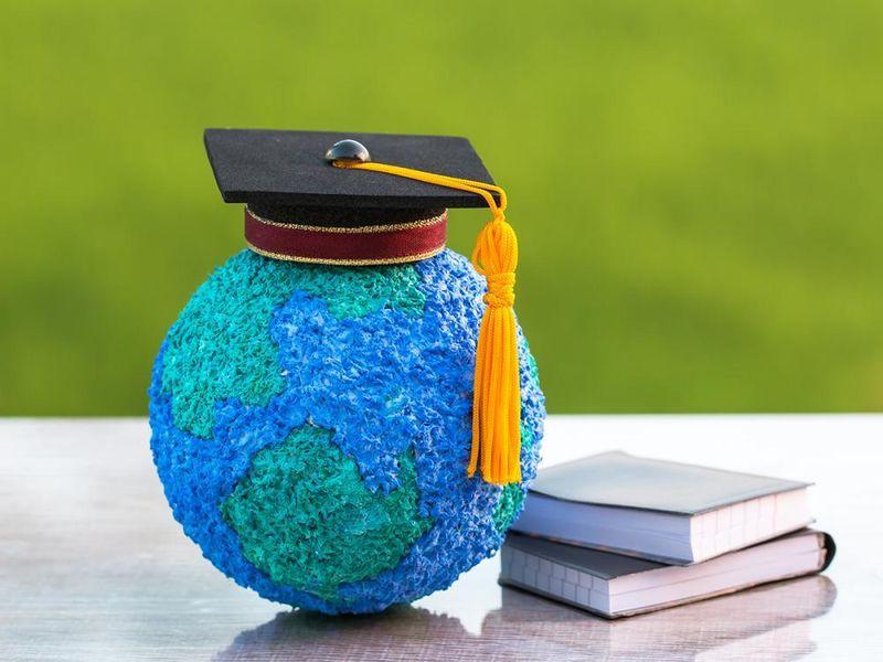 A small globe with a graduation cap on it sitting next to a pile of books